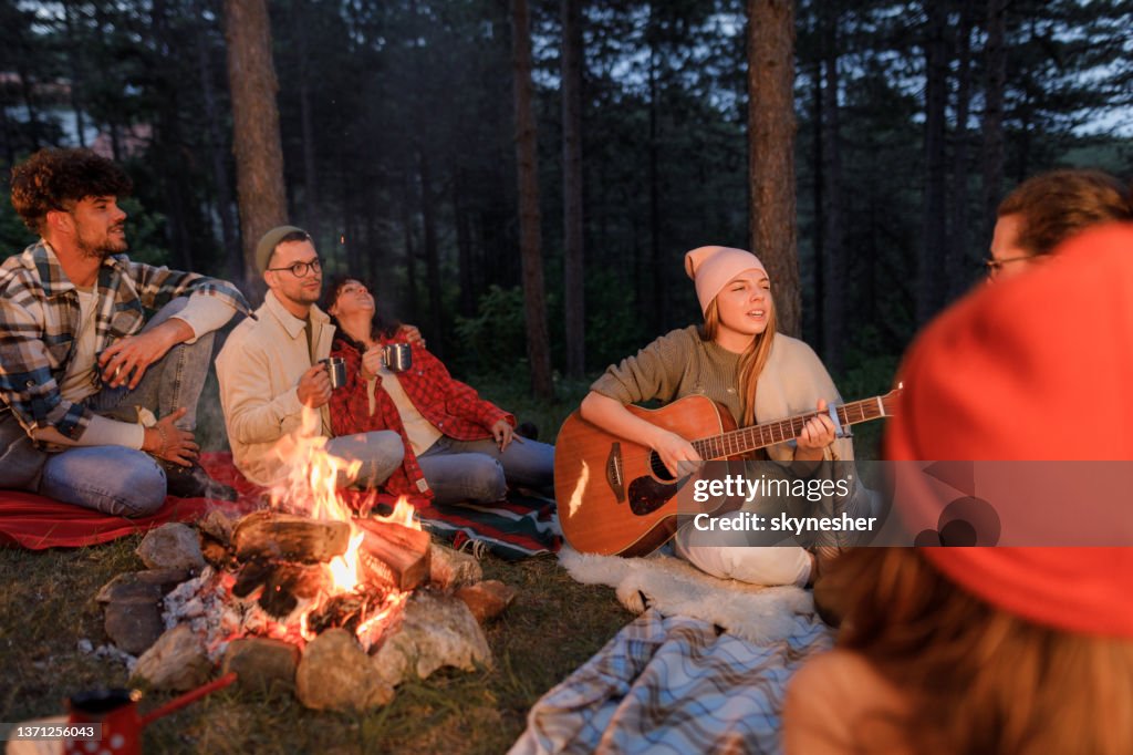 Joven tocando una guitarra a sus amigos en el campamento junto a la hoguera