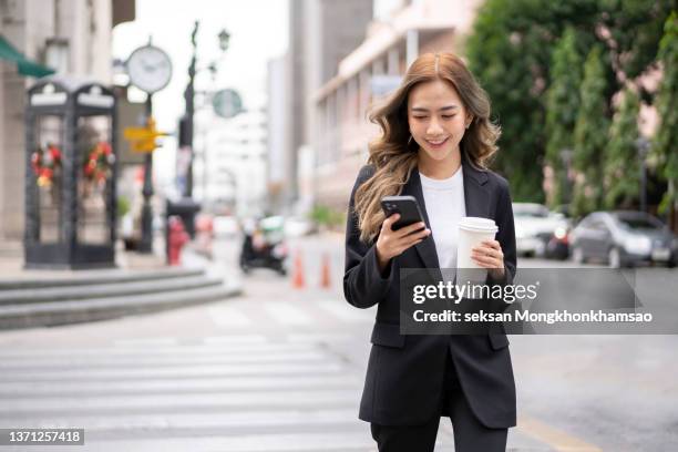 beautiful businesswoman holding reusable mug and talking on smart phone while walking in street in city. - fashionable businesswoman stock pictures, royalty-free photos & images