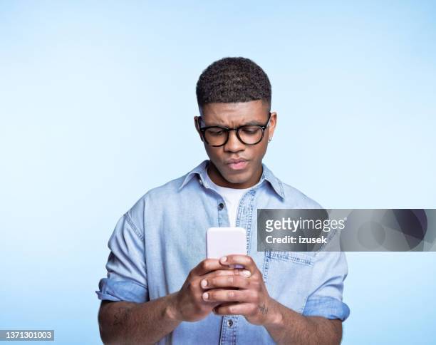 confused young man using smart phone - cell phone confused stockfoto's en -beelden