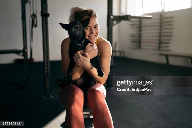 joyful caucasian sportswoman embracing her dog in the gym - form fitted stock pictures, royalty-free photos & images