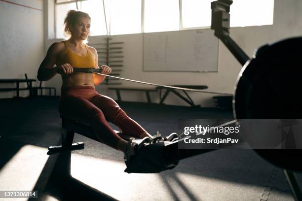 at the gym, strong caucasian woman exercising on the rowing machine - rowing machine stock pictures, royalty-free photos & images