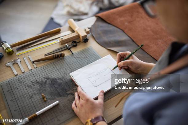 artisan du cuir réalisant un croquis pour portefeuille en atelier - maroquinerie photos et images de collection