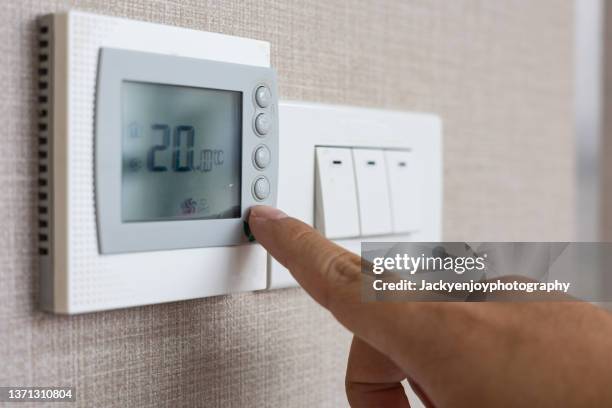 person adjusting a thermostat - aire acondicionado fotografías e imágenes de stock