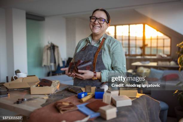 portrait d’une femme heureuse avec ses produits faits à la main dans son atelier d’artisanat du cuir - maroquinerie photos et images de collection