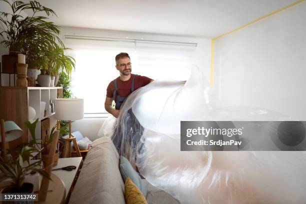 caucasian craft person, covering the furniture with protective plastic foil - man wrapped in plastic stock pictures, royalty-free photos & images