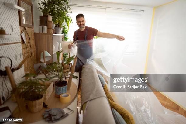 trabajador de la construcción masculino, cubriendo los muebles con lámina de plástico protectora - cubrir fotografías e imágenes de stock