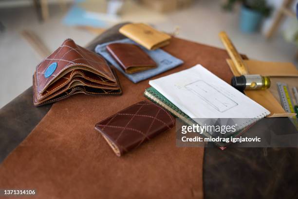 handmade leather wallets and sketch for new wallet on table in leather crafting workshop - leather notebook stock pictures, royalty-free photos & images