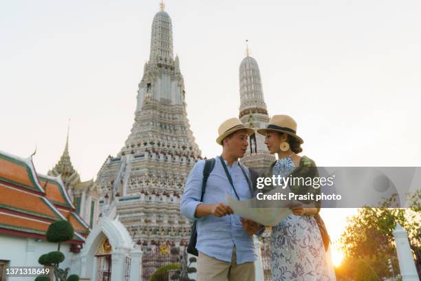 mixed race couple happy tourists to travel on they holidays and holding travel map and pointing in wat arun temple in bangkok, thailand"r - happy holidays around the world stock pictures, royalty-free photos & images