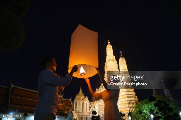 mixed race romantic lover couple in wat arun in night time and floating lamp in yi peng festival under loy krathong day, bangkok city ,thailand"r - yi peng - fotografias e filmes do acervo
