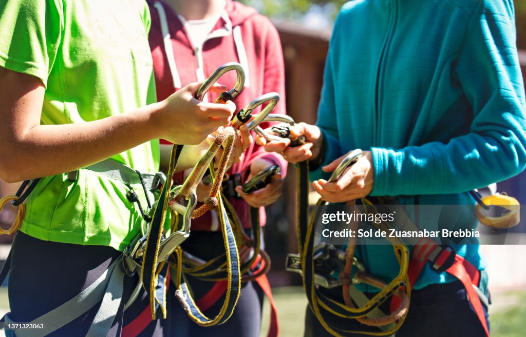 Group of teenagers (or mother and daugthers) ready for a day of adventures in a zip line park. The image shows a close-up of the safety carabiners