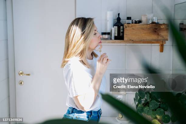 woman gives anti aging facial massage at home in the bathroom. woman massaging her face with a pink  quartz face roller.  facial skin care - aged to perfection stock pictures, royalty-free photos & images