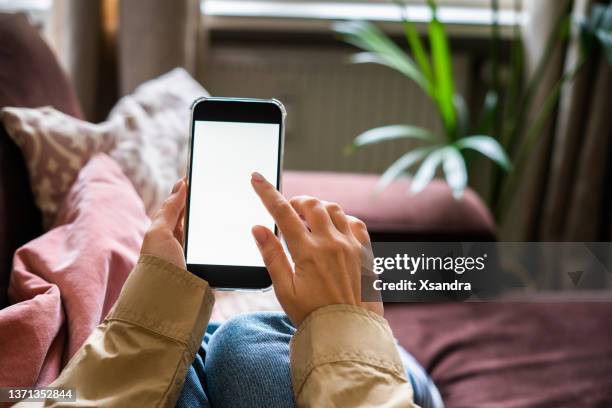 woman using smartphone with a blank screen in the living room at home - phone blank screen stock pictures, royalty-free photos & images