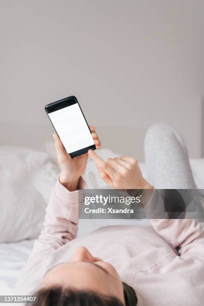 woman relaxing in bed and using a smartphone with a blank white screen - finger dialing touch tone telephone stock pictures, royalty-free photos & images