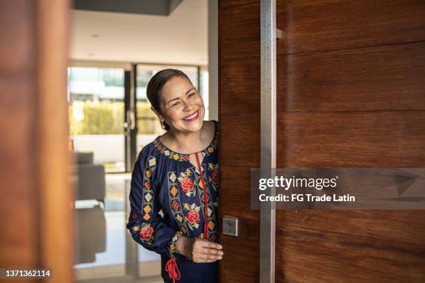 mature latin woman opening the front door - opening front door stock pictures, royalty-free photos & images