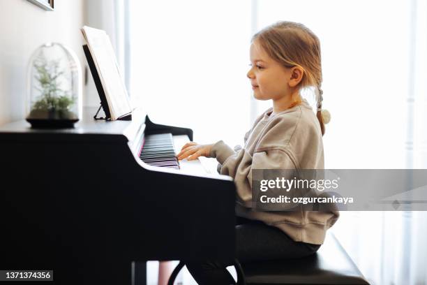 beautiful little toddler girl playing piano in living room. cute preschool child having fun with learning to play music instrument - keyboard white stockfoto's en -beelden