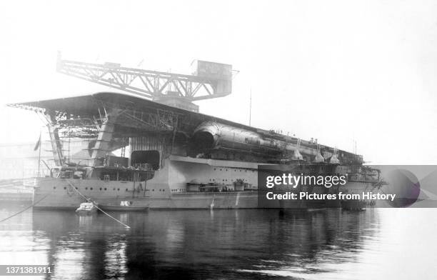 Imperial Japanese Navy aircraft carrier Kaga being fitted out in 1928. Note the distinctive long funnel below the flight deck and the three 8-inch...