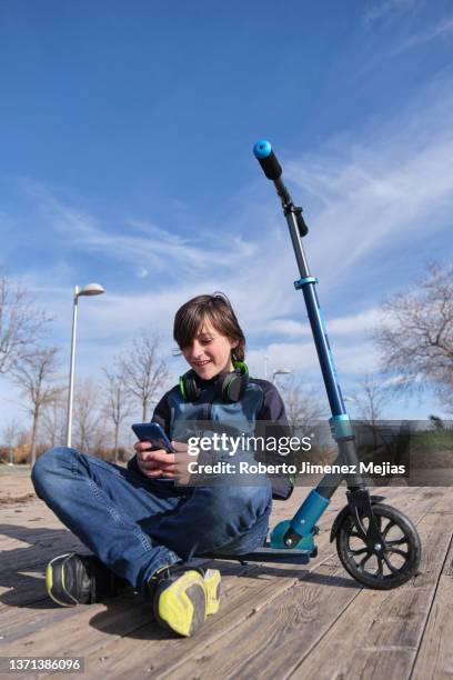 teenager sitting next to his scooter using a smart phone - elektro tretroller stock-fotos und bilder