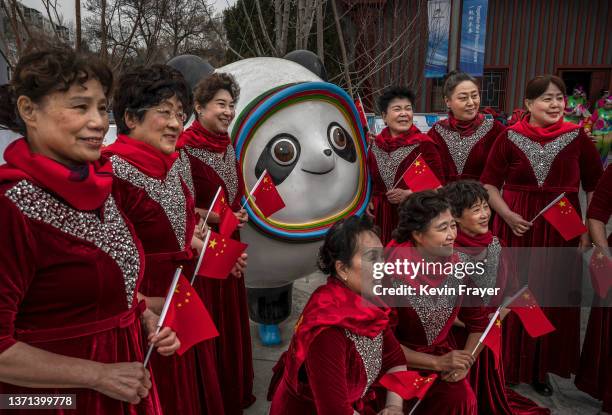 Women wear hold Chinese national flags as they stand with a statue of popular mascot Bing Dwen Dwen, before performing at a local community centre...