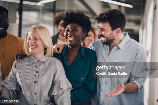 fröhliche junge menschen, die gemeinsam im gemeinsamen büroflur spazieren gehen - african american interview stock-fotos und bilder