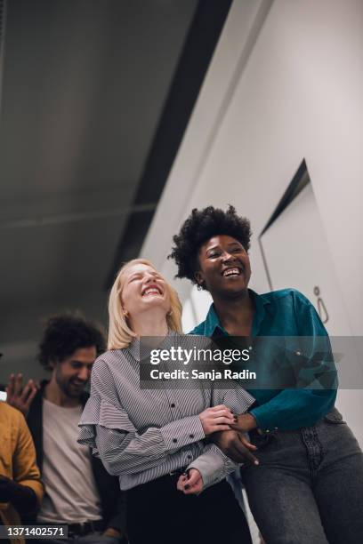 zwei junge kolleginnen lachen und haben spaß in ihren gemeinsamen büroräumen - african american interview stock-fotos und bilder