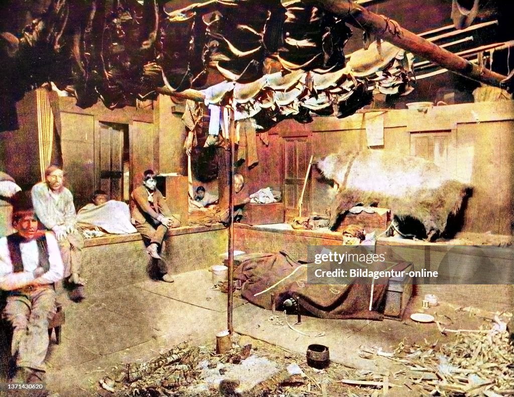 Inside an Indian hut in Yakutat Bay in Alaska, in the middle of the fire place and the family members sit or sleep distributed in the cottage.