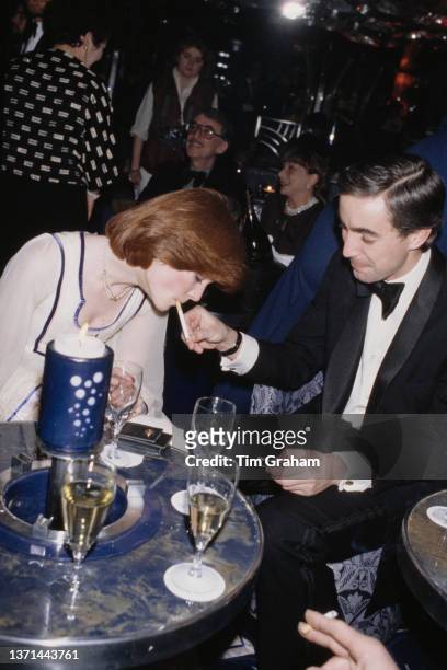 Lady Sarah Spencer has her cigarette lit by a man wearing a tuxedo at the opening of Regines, the nightclub at Kensington Roof Gardens in London,...