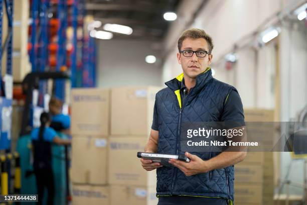 inventory management & tracking system. portrait of a male warehouse manager holding a digital tablet while standing in front of product in carton box at a distribution warehouse. he is an expert in planning and management in logistics and warehousing. - regular man stock pictures, royalty-free photos & images