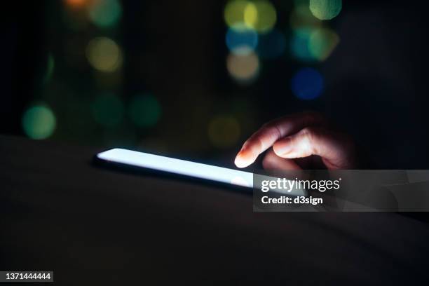 close up shot of female hand scrolling on smartphone device screen by the window at night, against illuminated bokeh light in the dark. lifestyle and technology - finger dialing touch tone telephone stock pictures, royalty-free photos & images