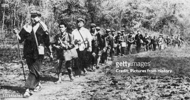 In a staged photograph, a troop of Khmer Rouge guerrillas file through the jungle of western Cambodia. Pol Pot strides out in the lead, followed by...