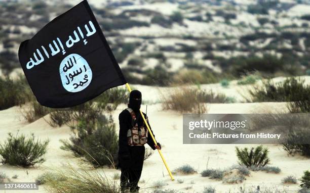 Islamic State/Iraq/Syria: A masked Islamic State soldier poses holding the ISIL banner somewhere in the deserts of Iraq or Syria. ISIL publicity...