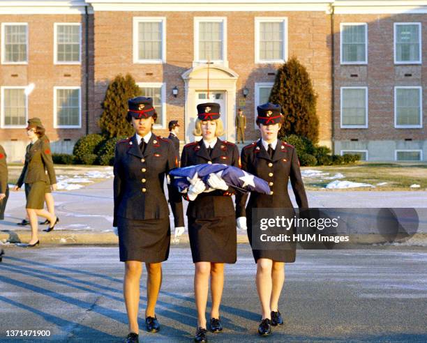 Three female Marines, in dress blue uniforms, raise the morning colors. First view in a series of three.