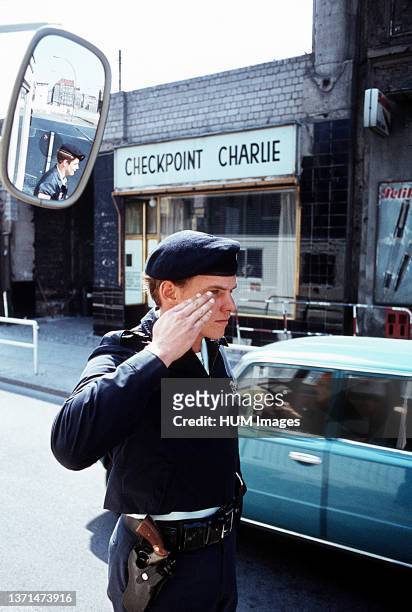 Security policeman, salutes a passing vehicle at Checkpoint Charlie, the allied entry point into East Berlin..