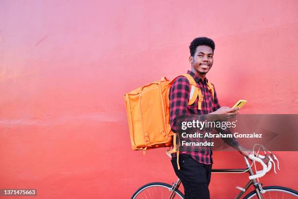 food delivery man holding mobile phone and looking away with his backpack and bicycle - man side way looking stock pictures, royalty-free photos & images