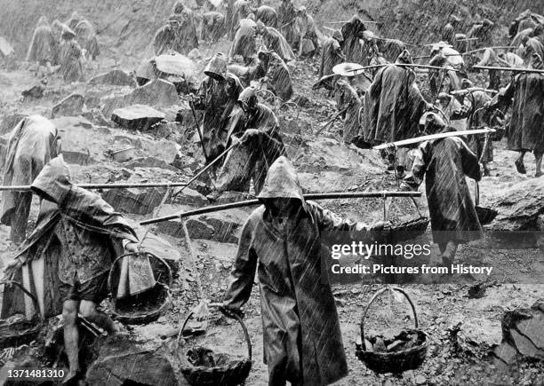 Team of workers labouring in a stone quarry in heavy rain during the 'Great Leap Forward' .