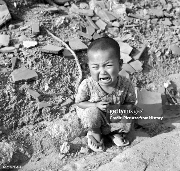 Japanese toddler sits crying amidst the rubble left by the explosion in Hiroshima following the dropping of the world's first atomic bomb on the city...