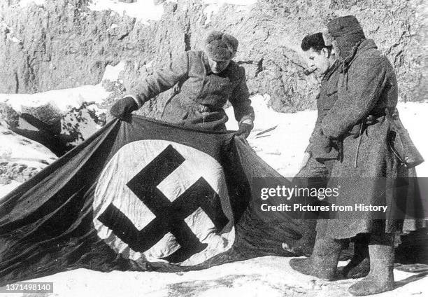 Warmly-clad Soviet soldiers inspect a captured Nazi flag, Stalingrad, February 1943.