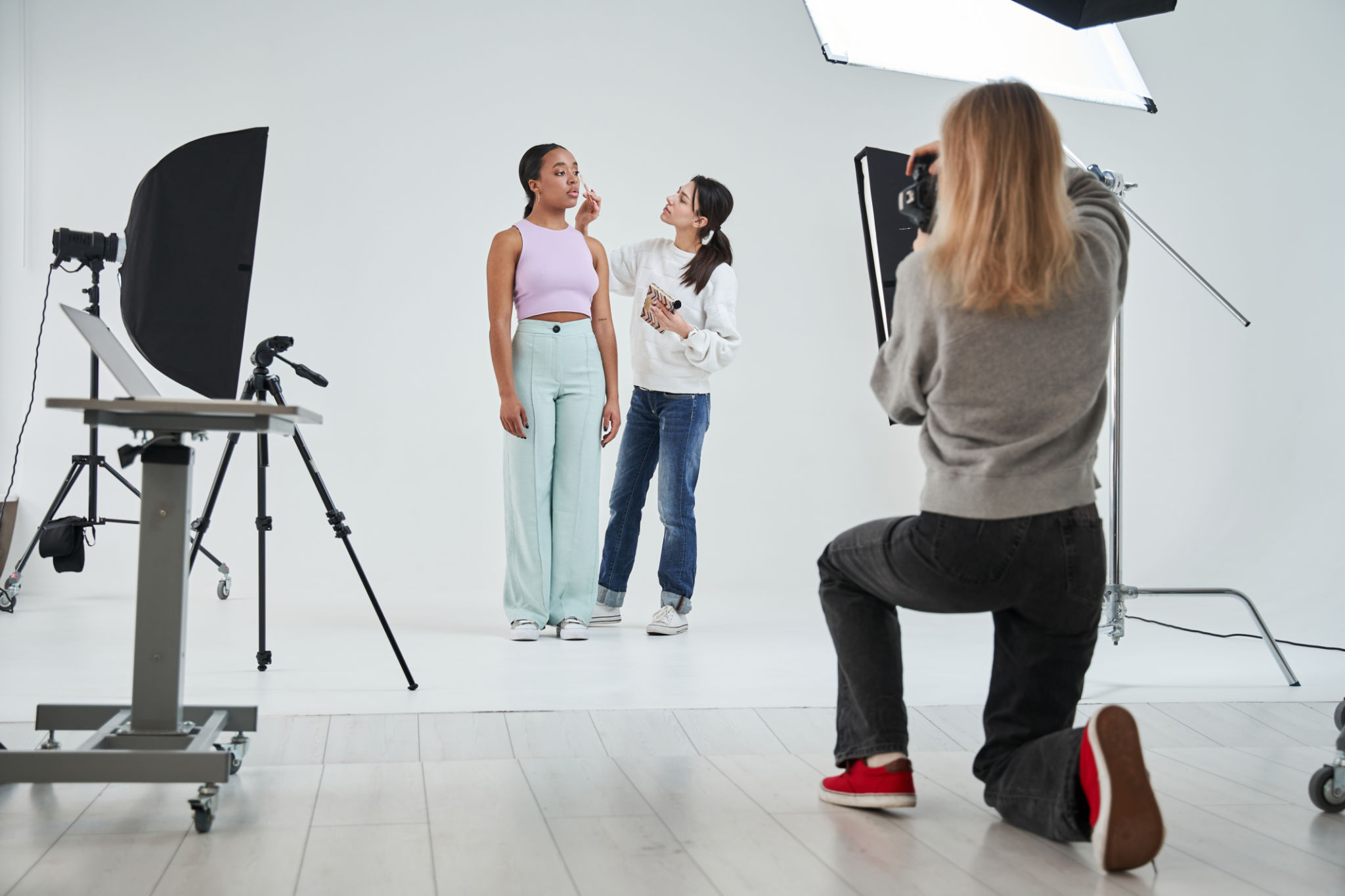 Make-up artist standing near the multiracial model and applying cosmetics Make-up artist standing near the multiracial model and applying cosmetics