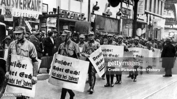 Nazi stormtroopers march with signs reading 'Germans Defend Yourselves - Don't Buy from Jews', 1938.