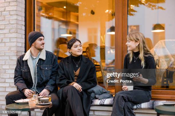 three friends sitting at street cafe talking while having coffee - berlin cafe stock pictures, royalty-free photos & images