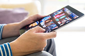Selective focus at men hand and digital tablet. Young Adult Asian man holding tablet device while choose online movie streaming application with mobile wireless network at home. Entertainment concept.