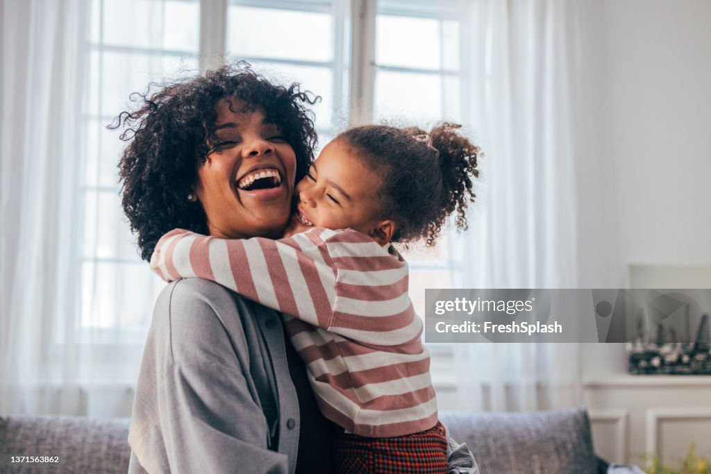 A Happy African-American Woman Being Hugged By Her Cute Little Daughter At Home