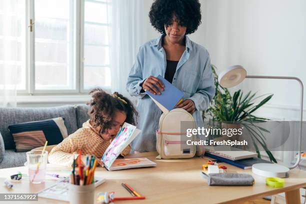 a cute little child sitting at the table at home yawning after doing her homework while her mother is helping her to prepare for school - yawning mother child stock pictures, royalty-free photos & images