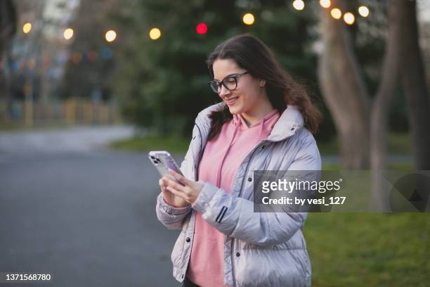 a teenage girl (16-17 years) in a park texting on her smart phone - 14 15 years girls stockfoto's en -beelden