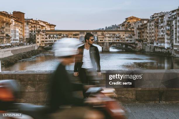 junger mann sitzt am fluss arno und genießt die aussicht in florenz, italien - vecchio stile stock-fotos und bilder