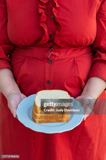 overweight lady wearing a dress with bulging buttons holding a plate of four slices of white bread - too small stockfoto's en -beelden