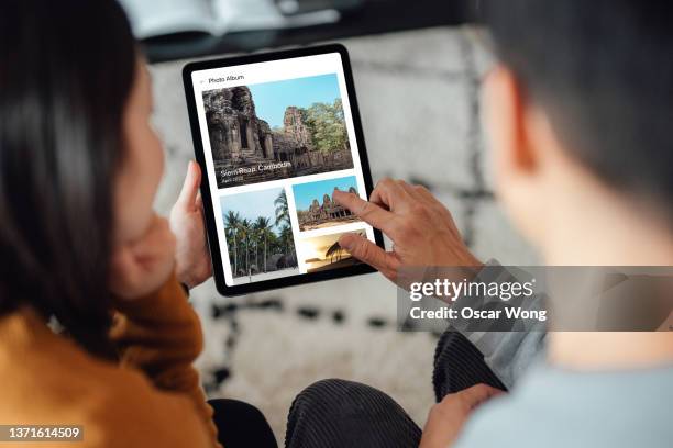 young couple looking at photo album on digital tablet - tablet screen stockfoto's en -beelden