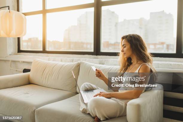 young woman relaxing on sofa and shopping online with  credit card and laptop - high tech beauty stockfoto's en -beelden