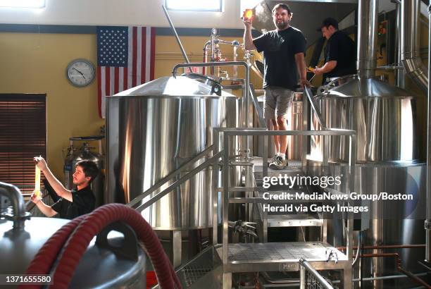 Jeff Leiter founder and brewer holds up some Flag Raiser IPA as apprenticesNolan Carpenter, right and Craig Foley, below, help brew at Somerville...