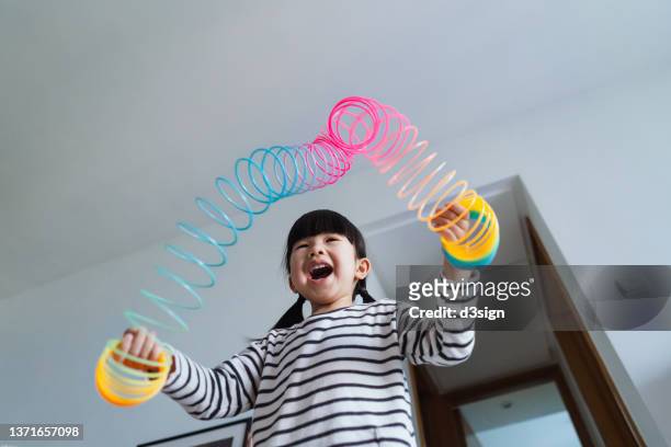 low angle shot of a joyful little asian girl playing with a colourful magic spring rainbow toy at home. simple joy and happiness. learning through play concept - saut elastique photos et images de collection