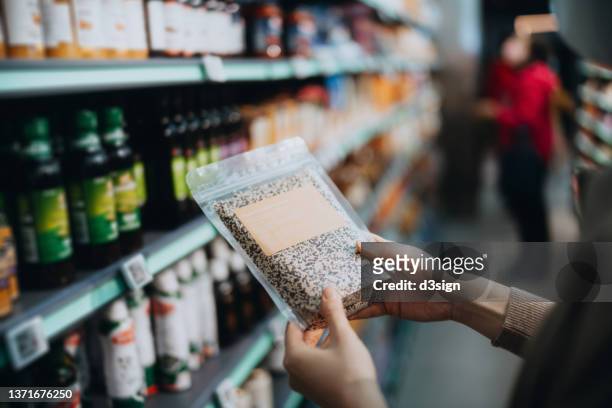 cropped shot of young asian woman grocery shopping for healthy food in a supermarket, holding a packet of organic tricolour quinoa and examining the nutrition values on the label. healthy eating lifestyle. making healthier food choices - natuurkunde stock-fotos und bilder
